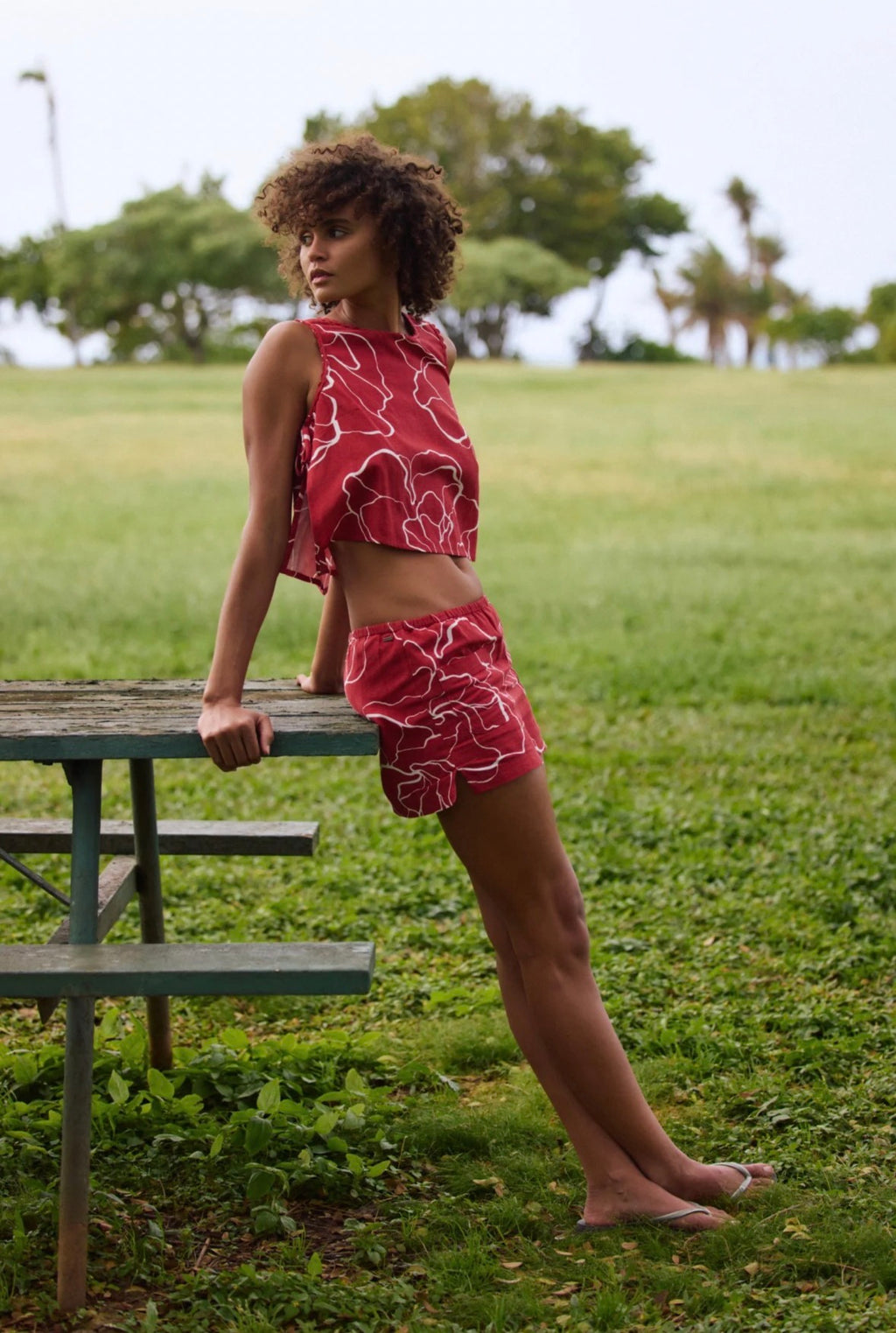 Woman in a red patterned outfit standing on grass with trees in the background