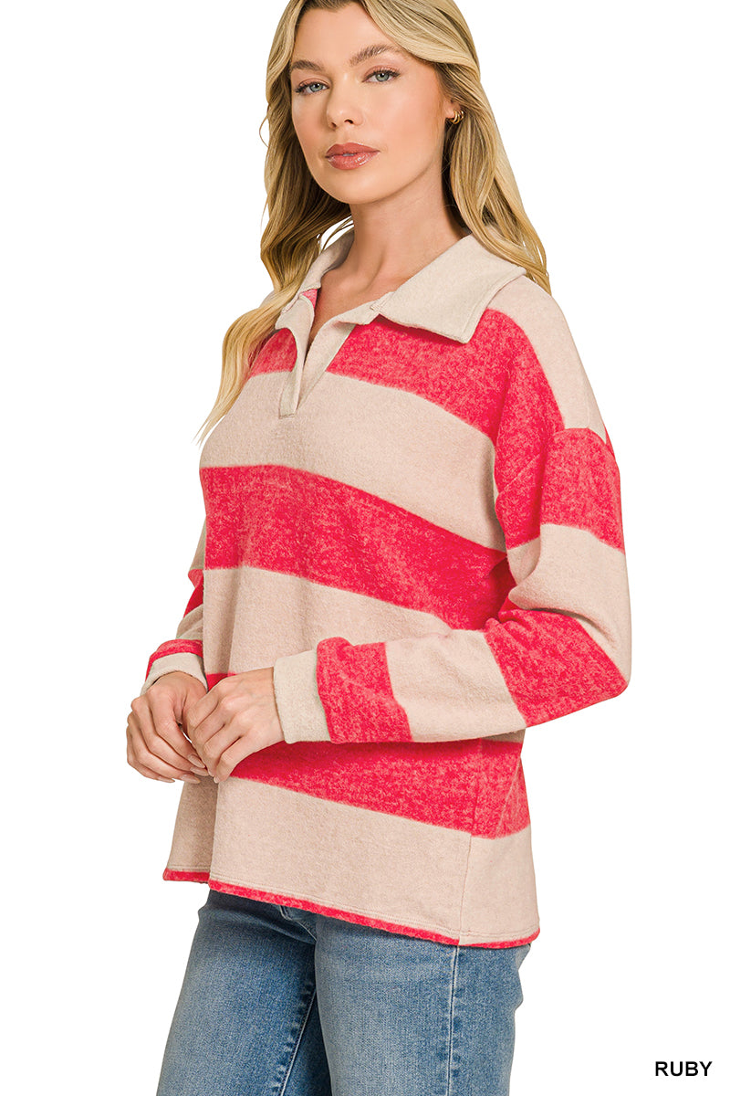 A woman wearing a long-sleeve collared knit top with bold horizontal stripes in red and beige, paired with blue jeans, against a plain white background.