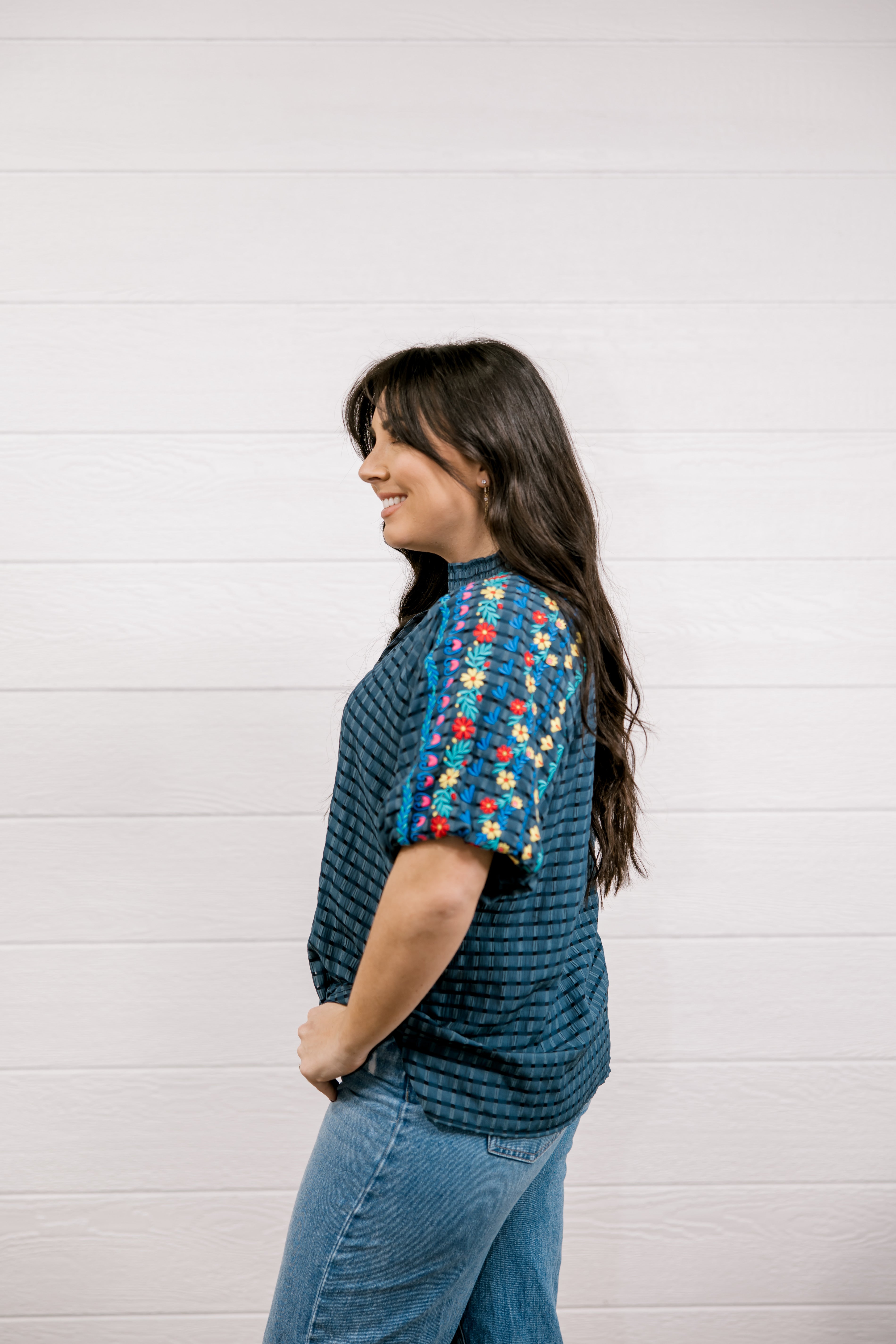 Woman wearing a teal knit sweater with colorful floral patterns on a white background
