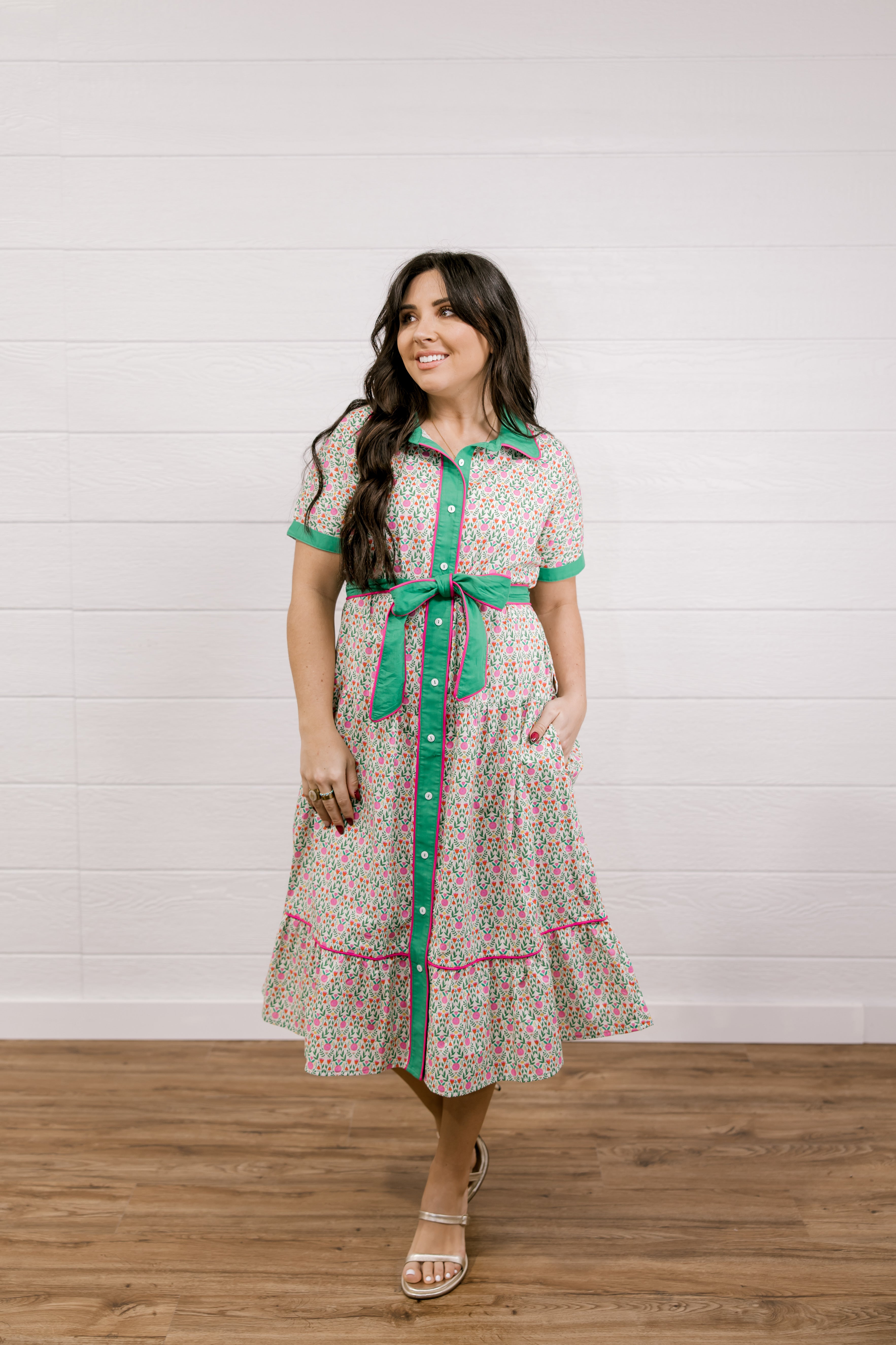 Woman wearing a patterned dress with a green belt against a white wooden panel background