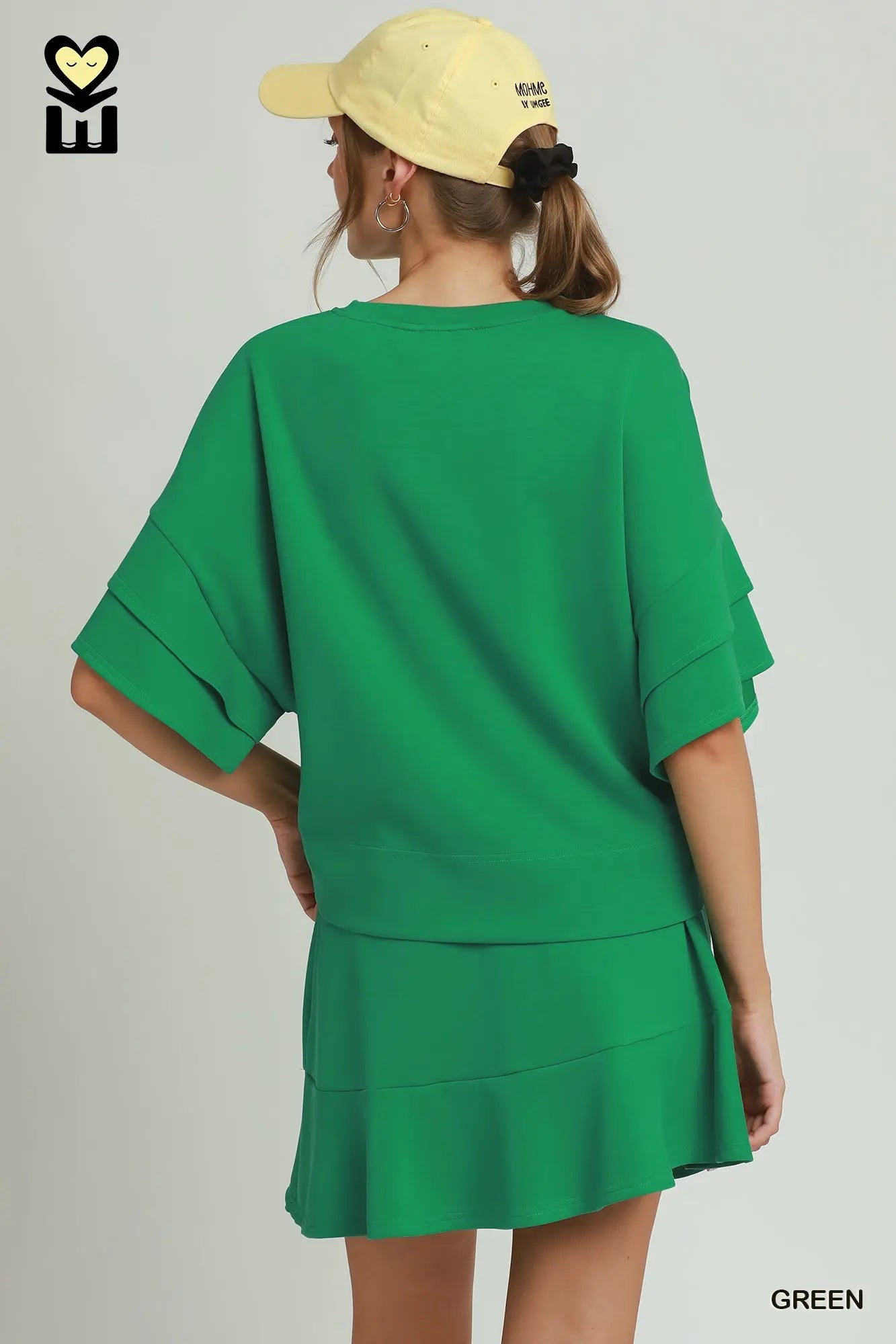 Person wearing a green dress and yellow cap on a plain background