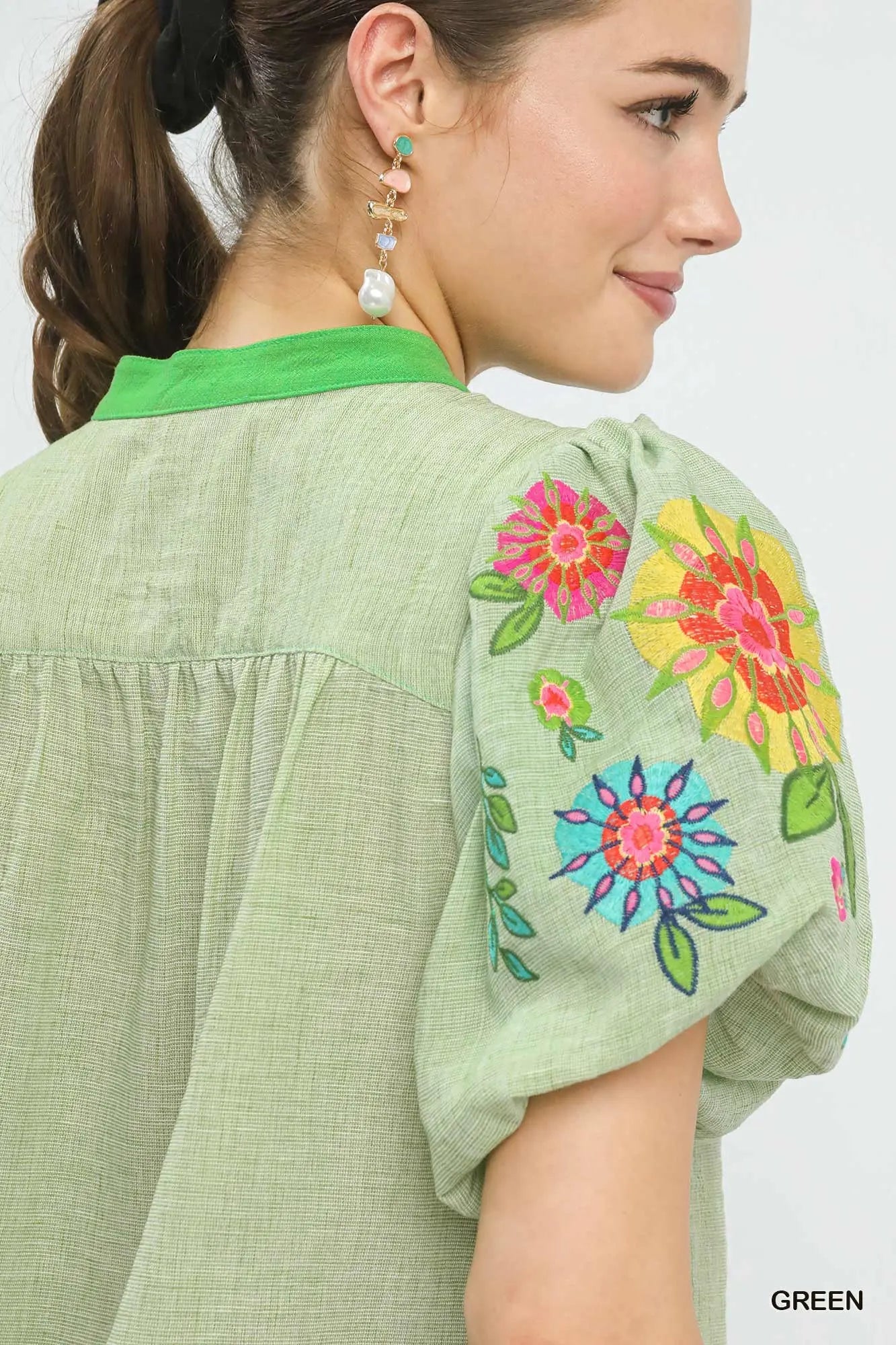 Woman wearing a green blouse with colorful floral embroidery on a plain background