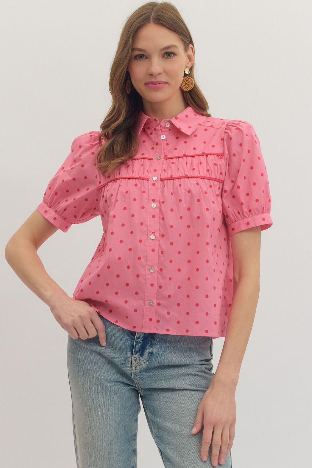 Woman wearing a pink polka dot blouse and blue jeans on a plain background