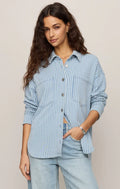 Woman wearing a blue striped shirt and light jeans against a beige background