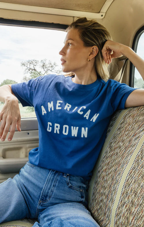 Woman wearing a blue 'American Grown' t-shirt sitting inside a vehicle.