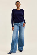 Woman wearing a navy sweater and blue jeans on a beige background