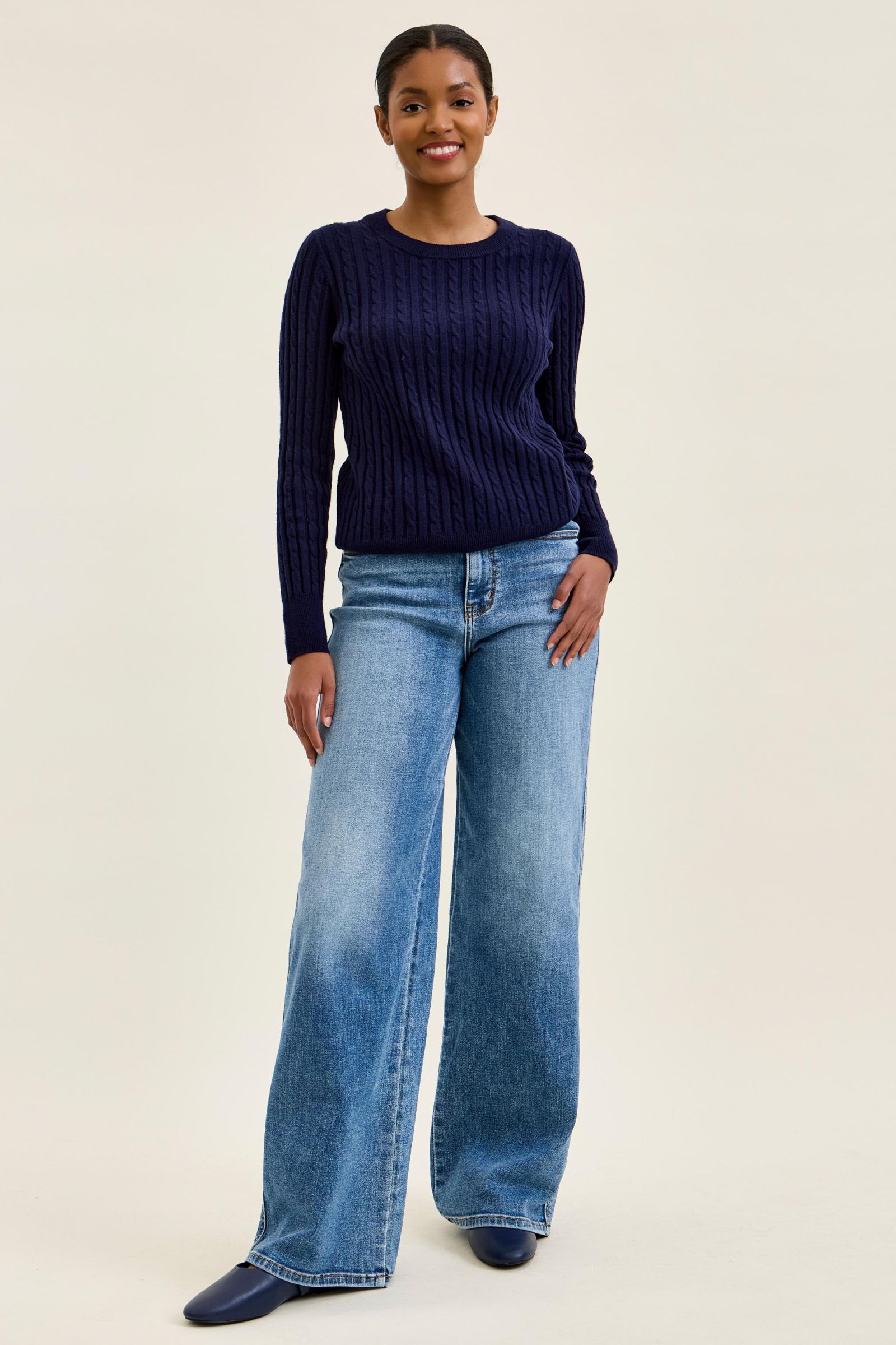 Woman wearing a navy sweater and blue jeans on a beige background