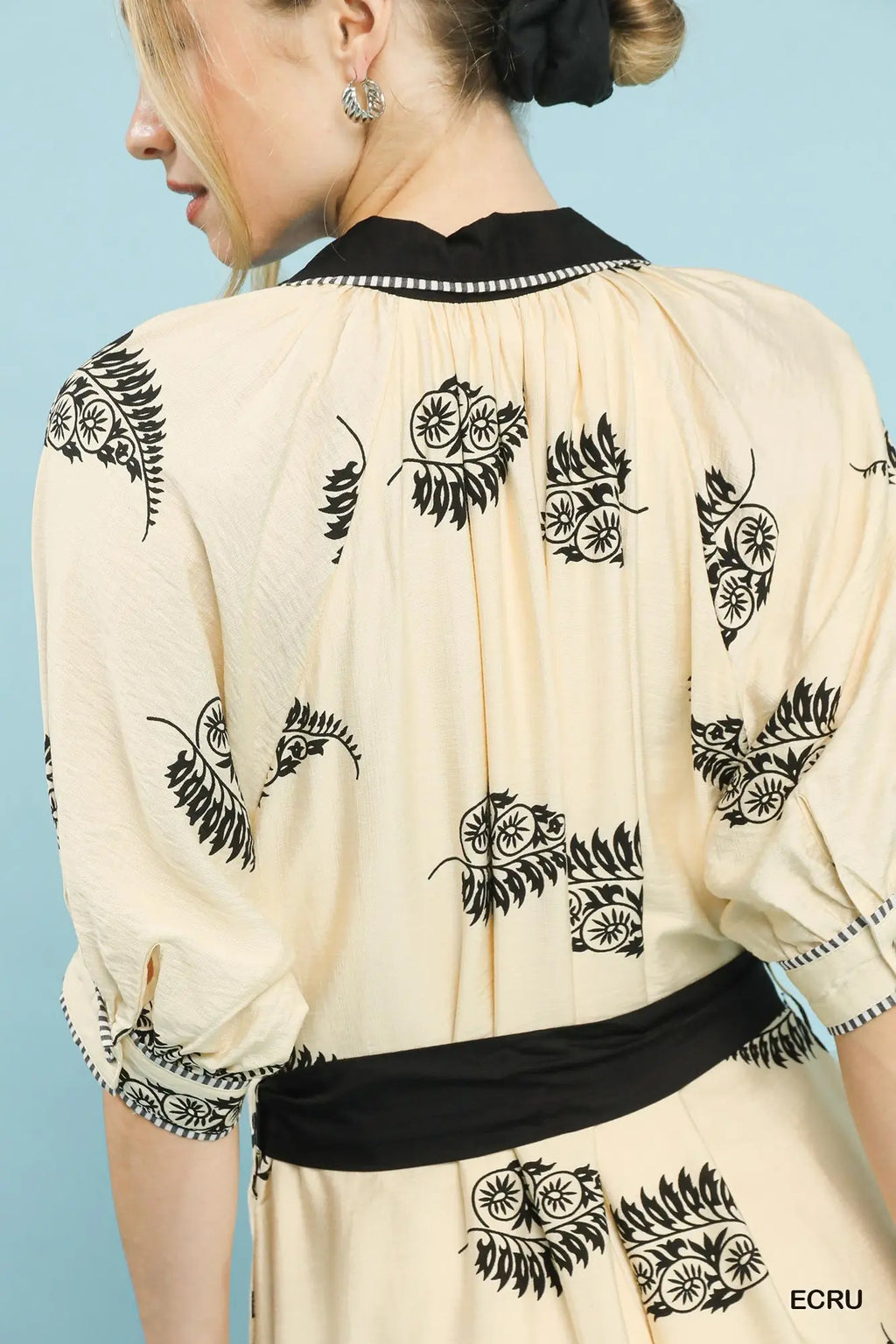 Beige dress with black floral patterns and a black belt against a light blue background