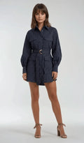 A woman modeling a navy blue and white vertically striped belted shirt dress with long balloon sleeves, a button-up collar, and front flap pockets, paired with beige ankle-strap high heels against a light gray studio background.