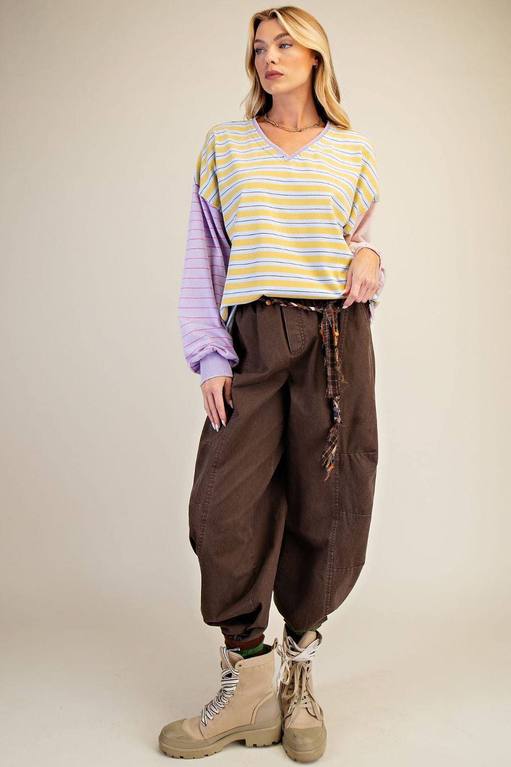 Woman wearing a striped shirt and brown pants against a beige background