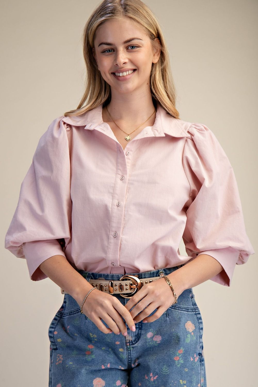 Woman wearing a pink blouse and floral jeans against a plain background