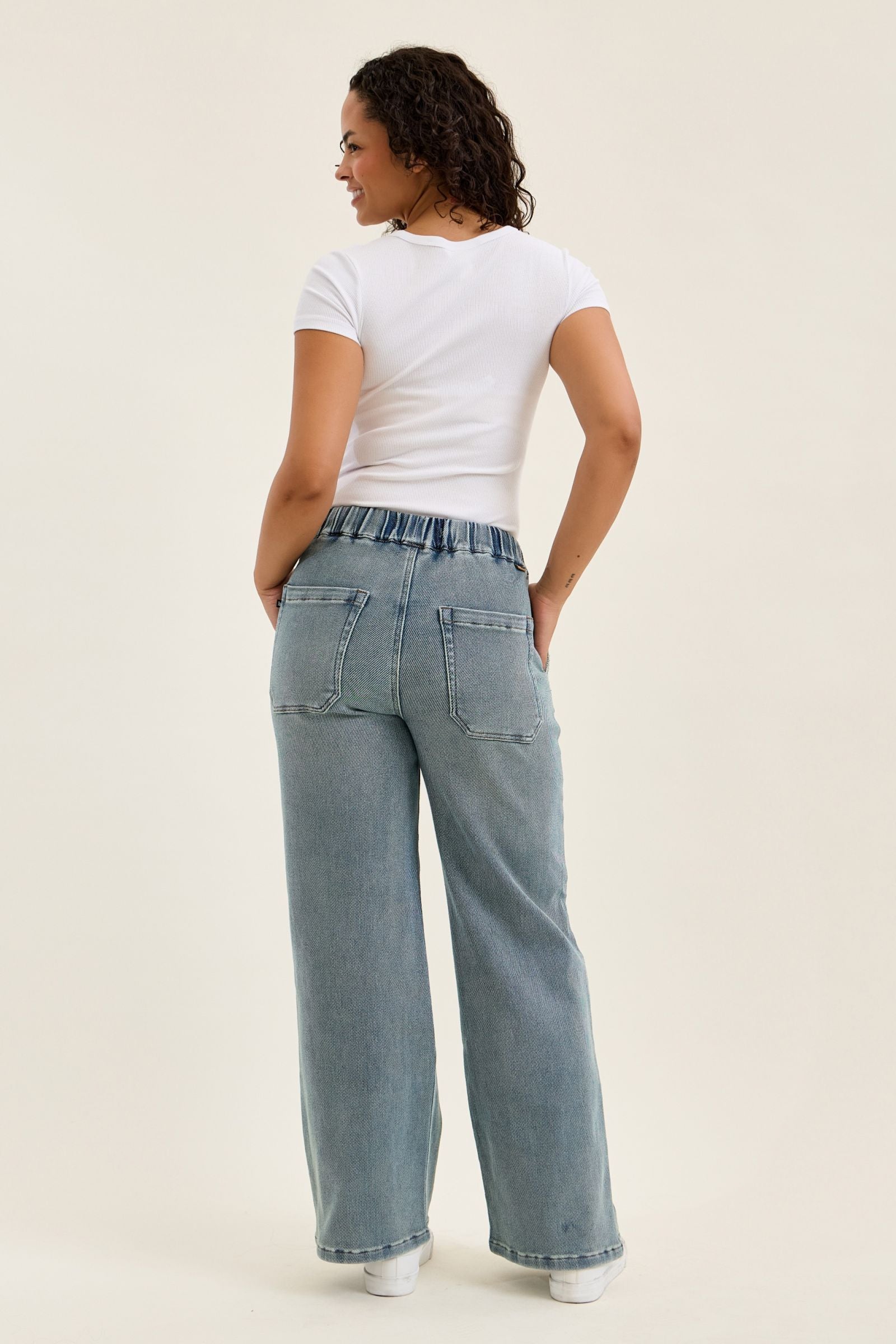 Woman wearing light blue jeans and a white t-shirt on a beige background