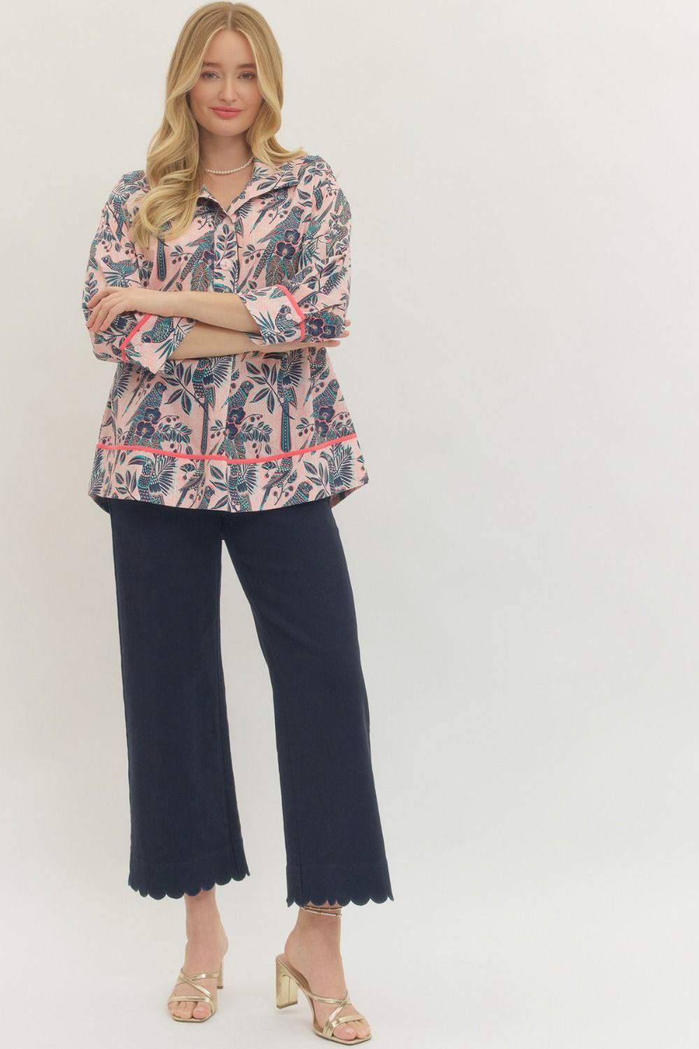Woman wearing a patterned blouse and navy pants on a white background