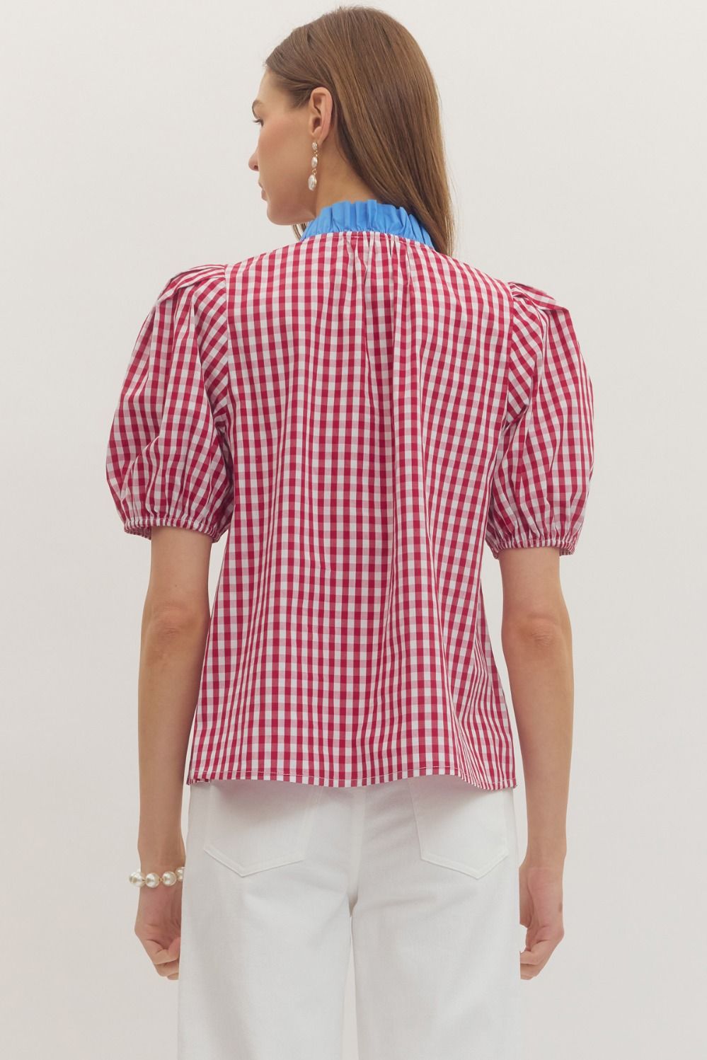 Woman wearing a red and white checkered blouse with blue collar on a plain background