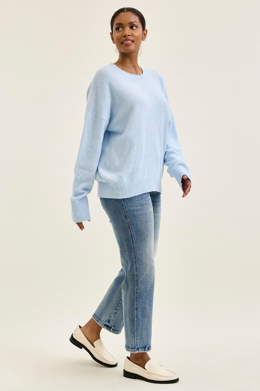 Woman wearing a light blue sweater and jeans on a beige background
