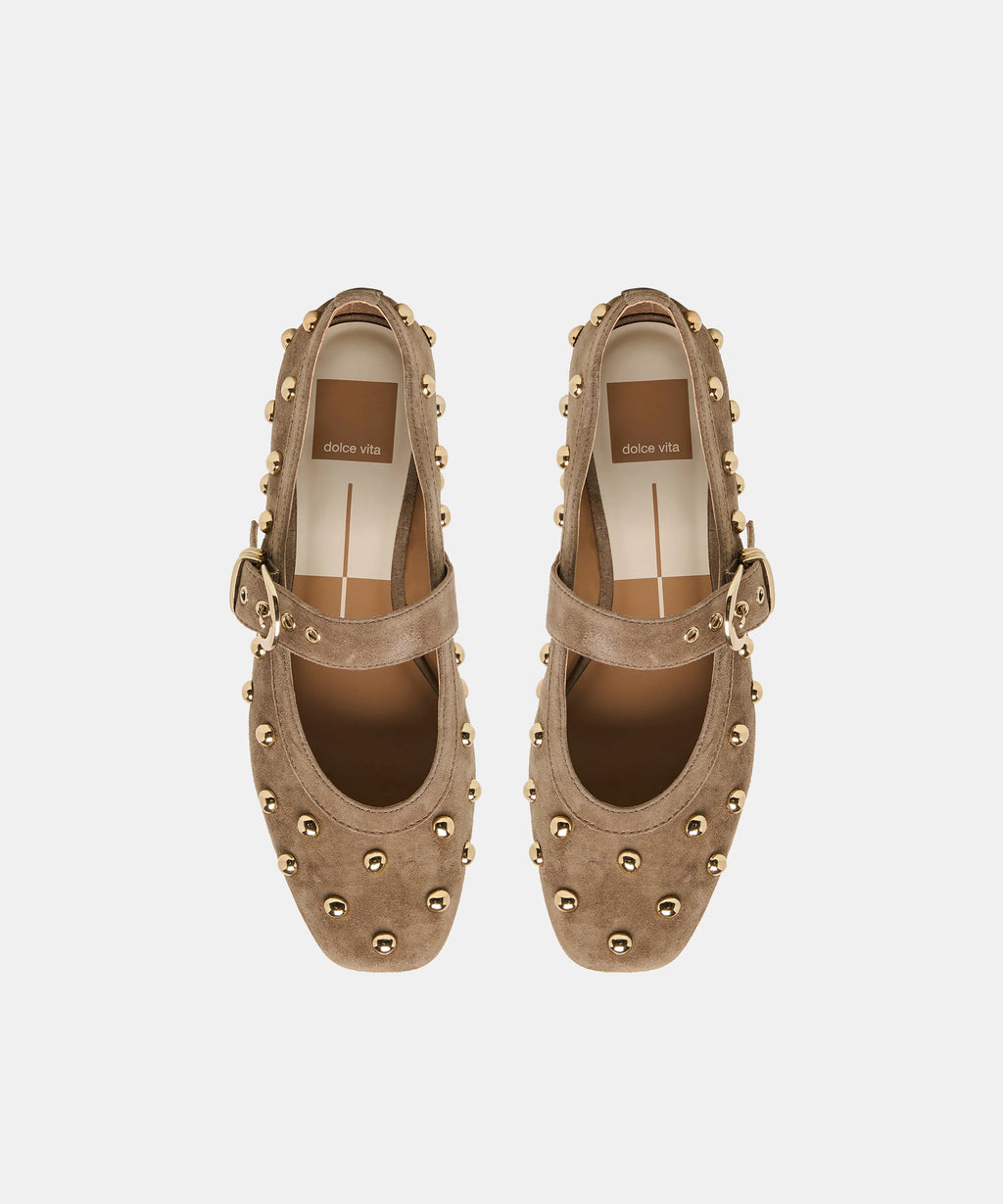 A pair of taupe-brown suede Mary Jane shoes with gold-tone studs and buckle straps, shown from a top-down view on a light gray background.
