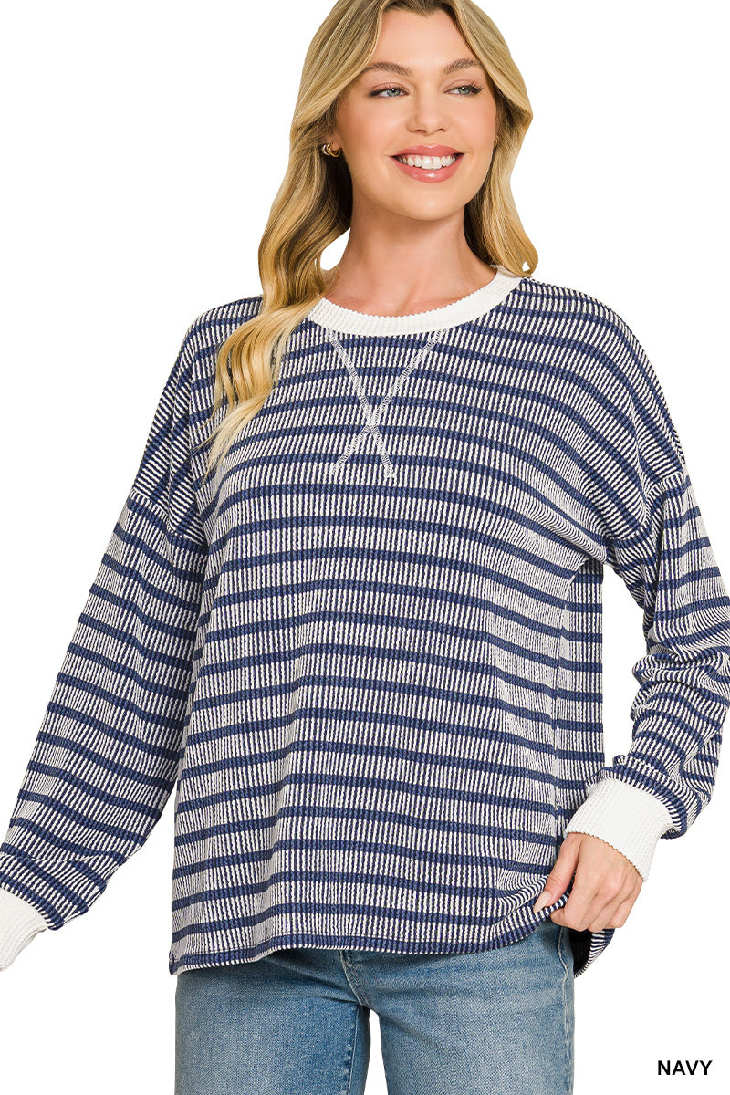 A woman wearing a navy and off-white horizontally striped knit sweater with a white crew neck and cuffs, paired with blue jeans, against a plain white background.