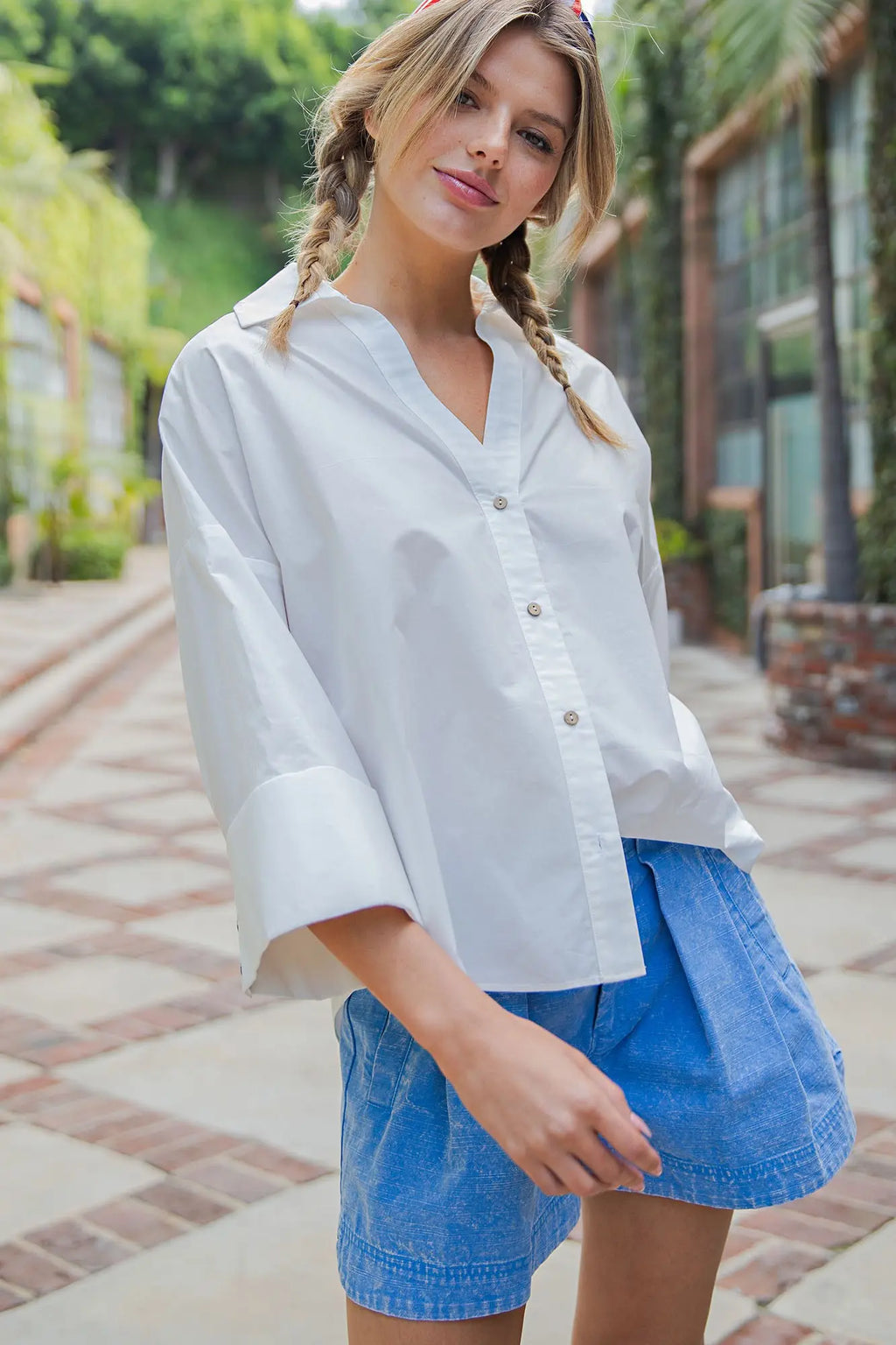 Woman wearing a white shirt and blue shorts standing outdoors on a brick path.