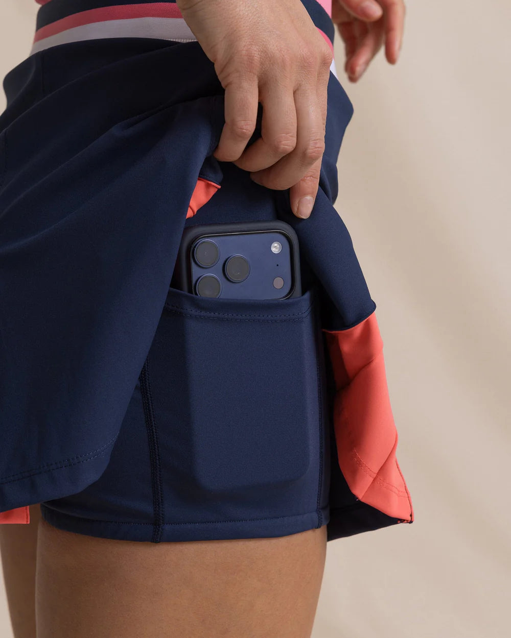 Person wearing navy shorts with a phone pocket holding a smartphone.
