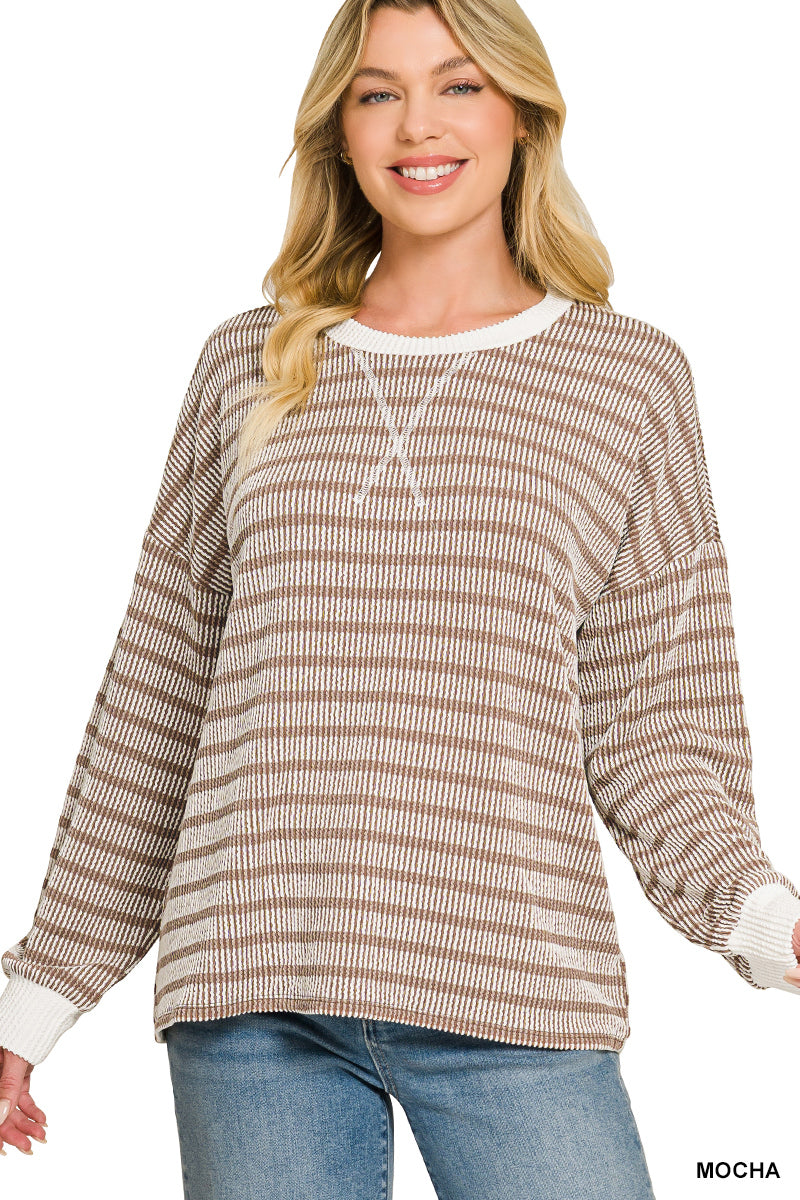 A woman wearing a long-sleeve waffle-knit sweater with horizontal taupe and cream stripes, featuring a white crew neck and cuffs, paired with blue jeans against a white background.