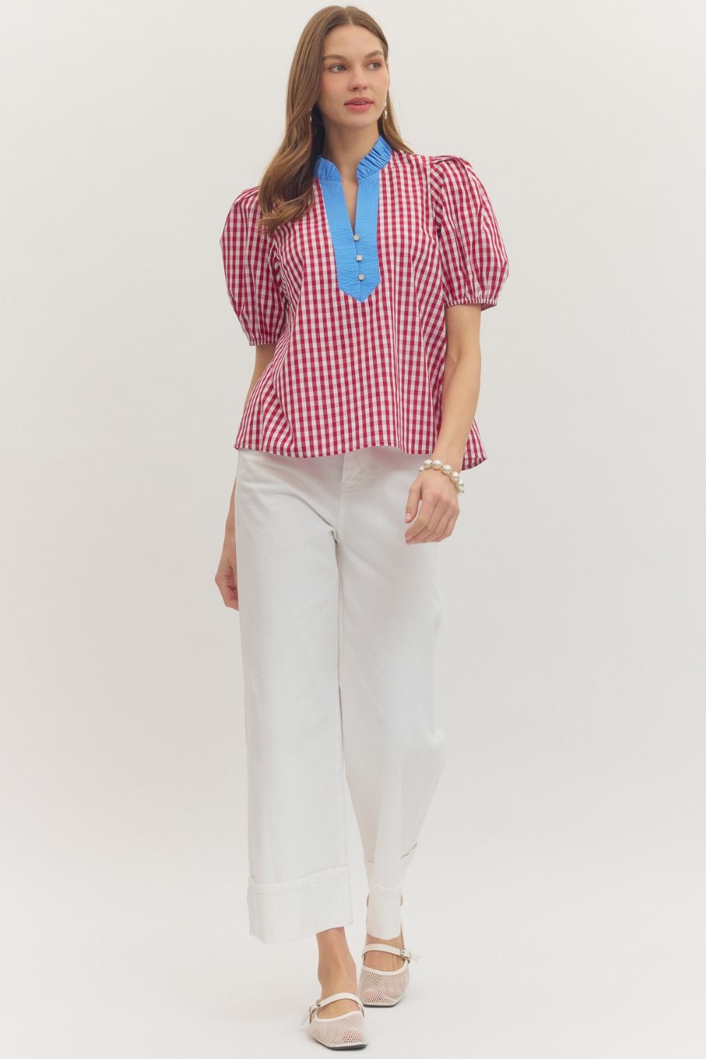 Woman wearing a red and white checkered blouse with blue accents and white pants on a white background