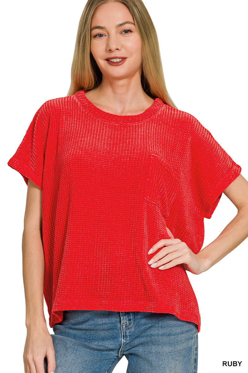 A woman modeling a short-sleeve, loose-fitting textured knit top in a vibrant red color, paired with blue jeans against a plain white background.