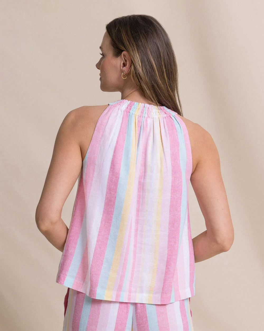 Woman wearing a pastel striped sleeveless top against a beige background