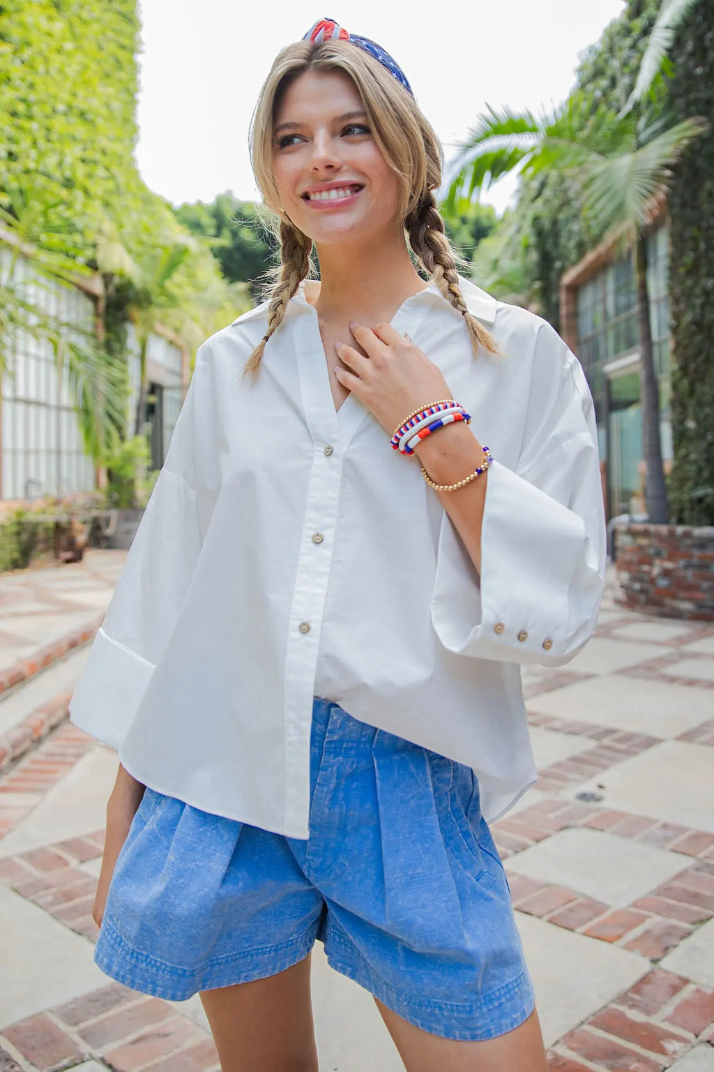 Woman wearing a white blouse and blue shorts in an outdoor setting with greenery.