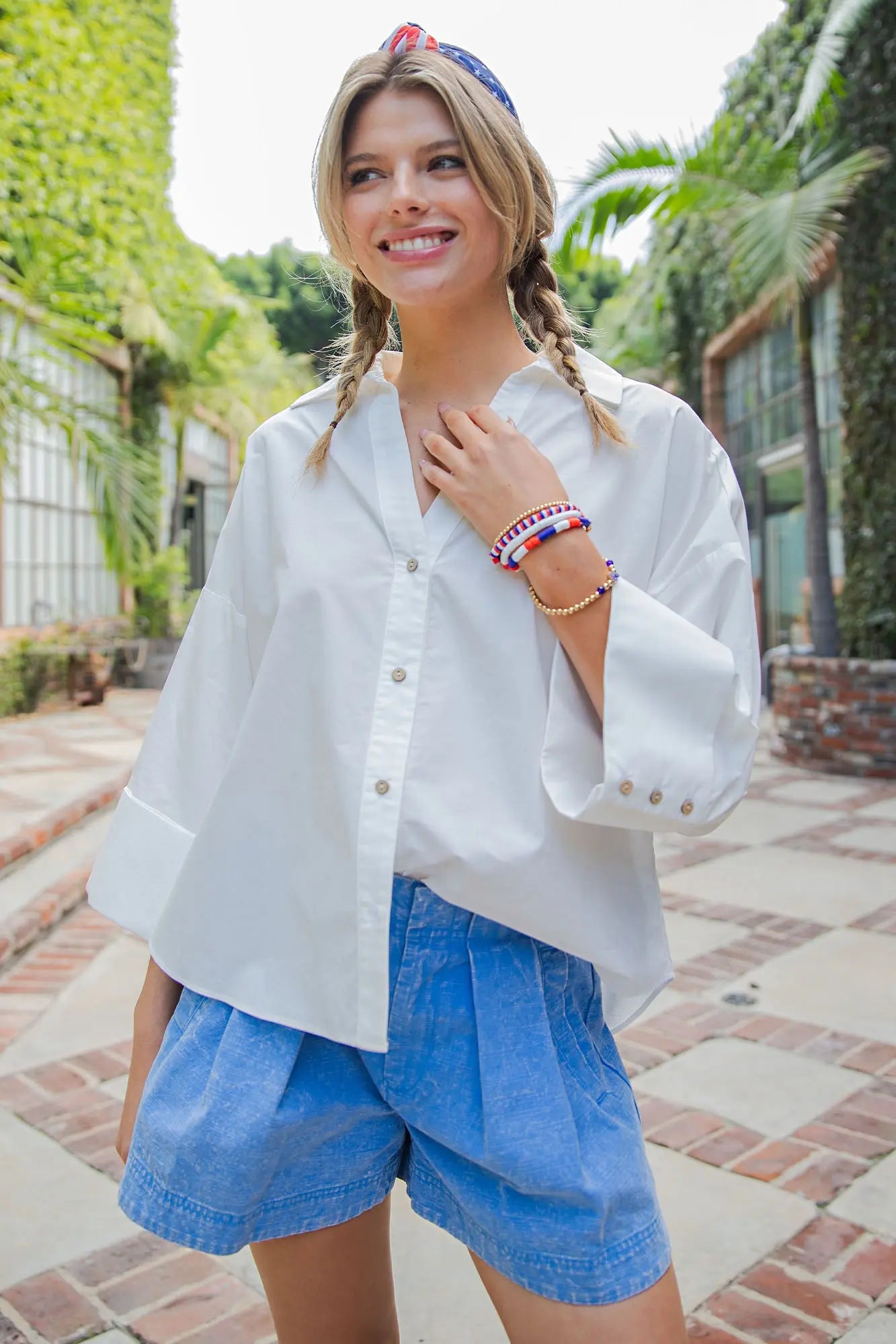 Woman wearing a white blouse and blue shorts in an outdoor setting with greenery.
