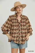 A woman modeling a bohemian-style long-sleeve blouse with a brown, beige, and red paisley pattern, paired with denim shorts and a tan wide-brim hat against a light gray background.