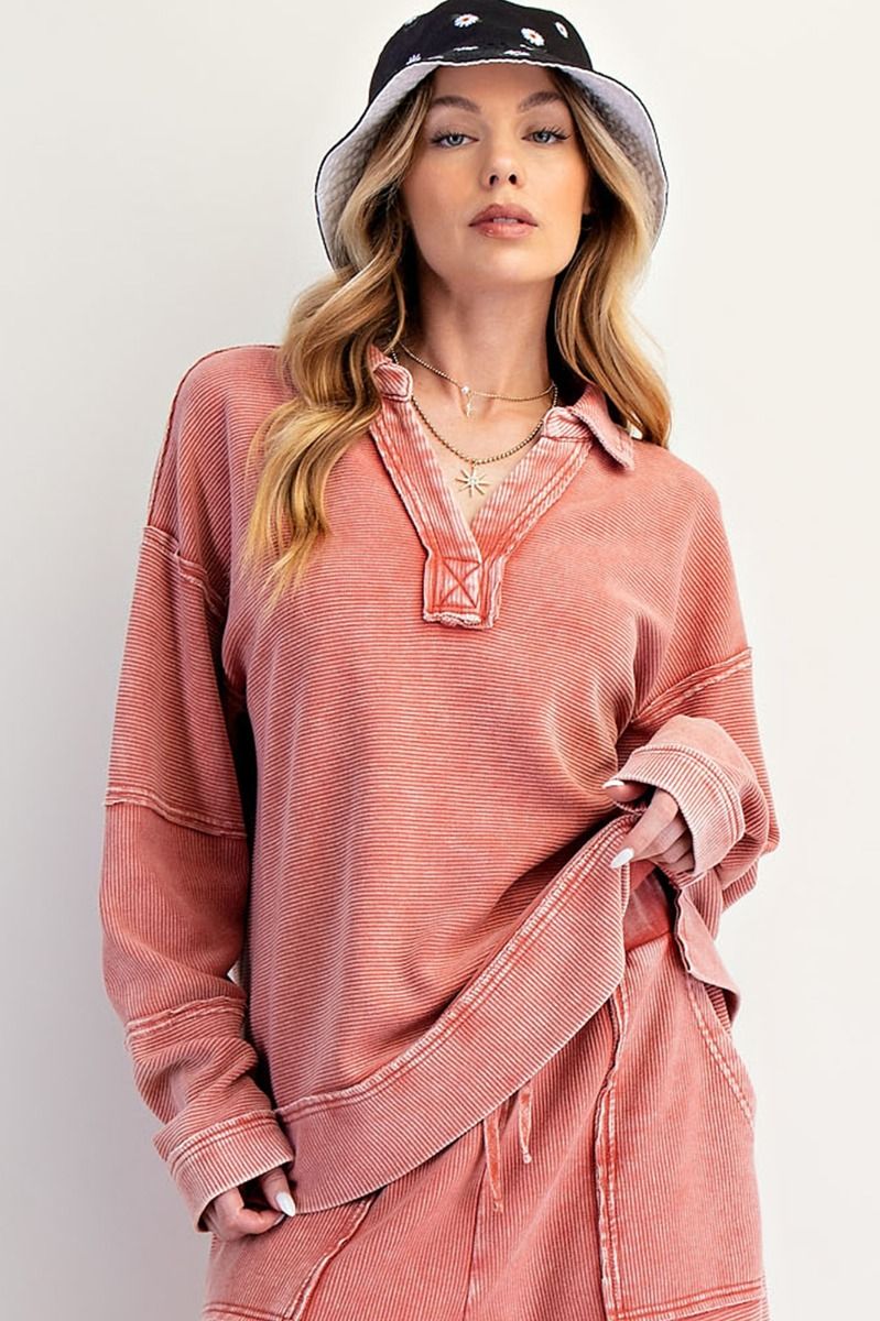 Woman wearing a pink oversized shirt and black and white bucket hat on a plain background