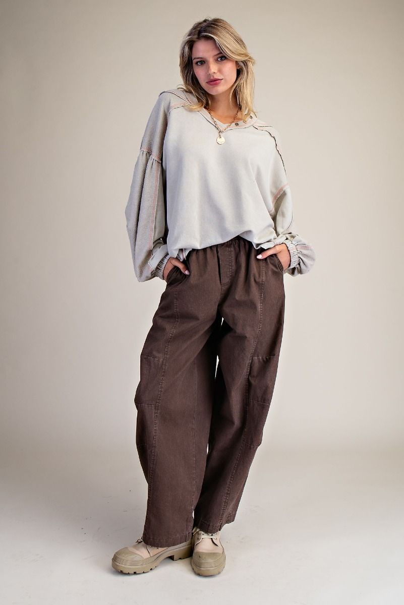 Woman wearing a white blouse and brown pants against a plain background