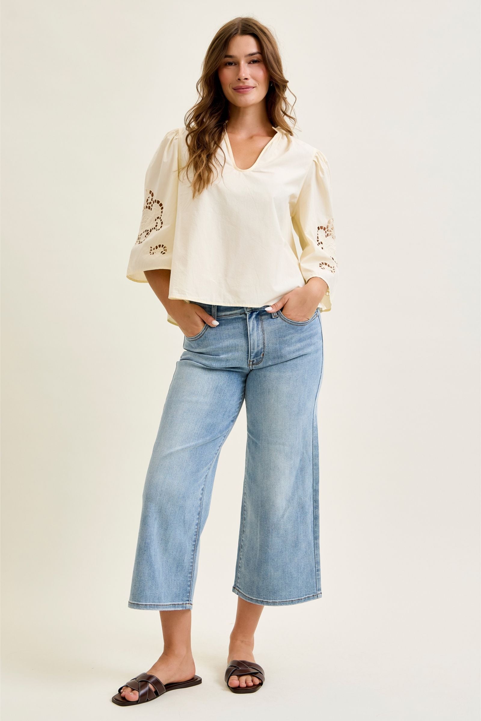 Woman wearing a cream blouse with floral embroidery and blue jeans on a white background