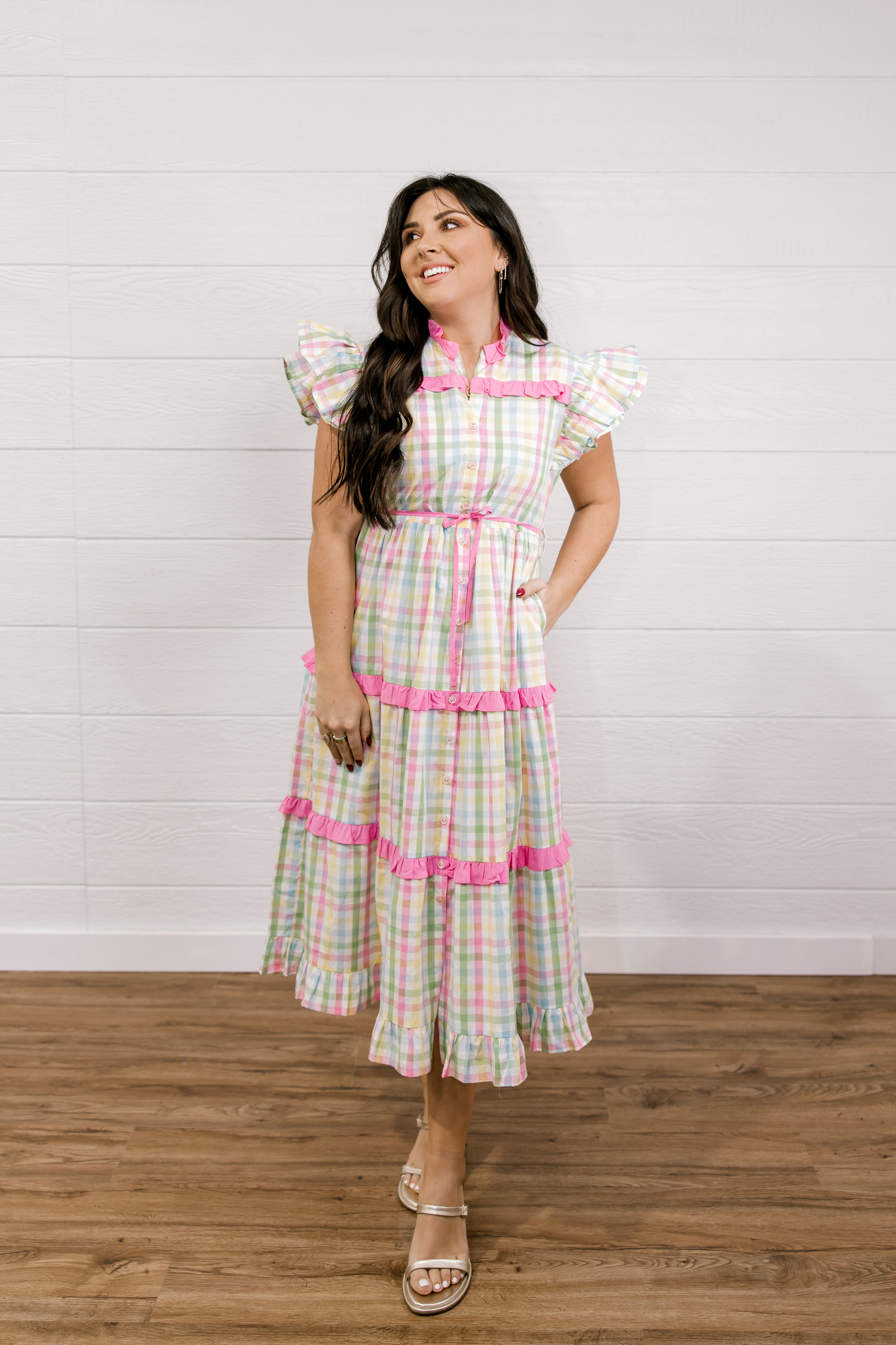 Woman wearing a checkered dress with pink accents against a white wall.