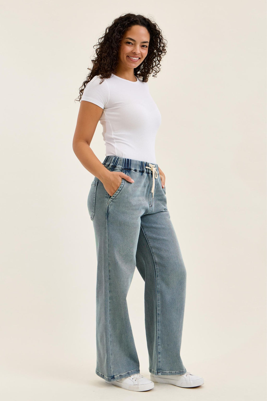 Woman wearing light blue jeans and a white t-shirt on a plain background