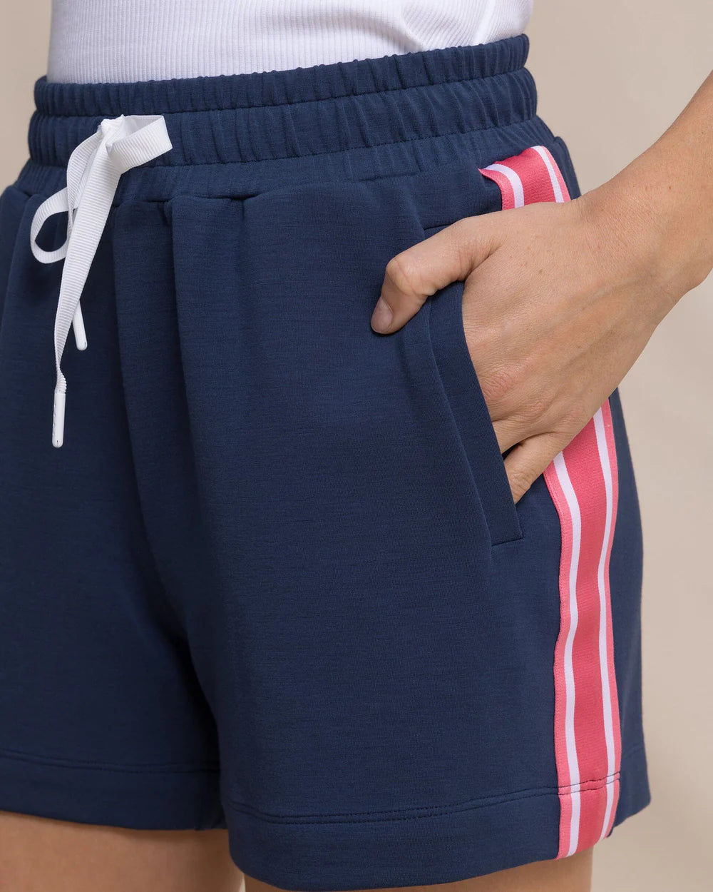 Navy shorts with a white drawstring and red and white striped side panel on a beige background