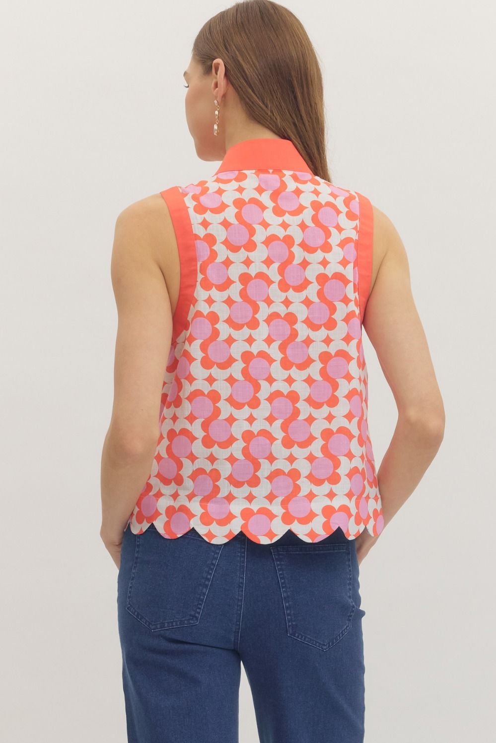 Woman wearing a sleeveless floral top with pink and orange pattern on a plain background