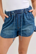 Blue denim shorts worn by a person on a plain background