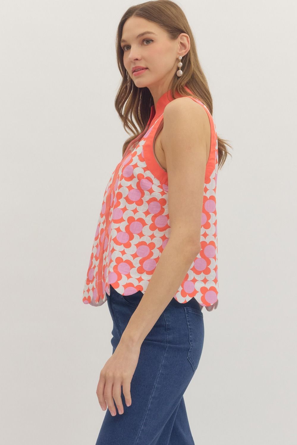Woman wearing a sleeveless floral top and blue jeans on a plain background