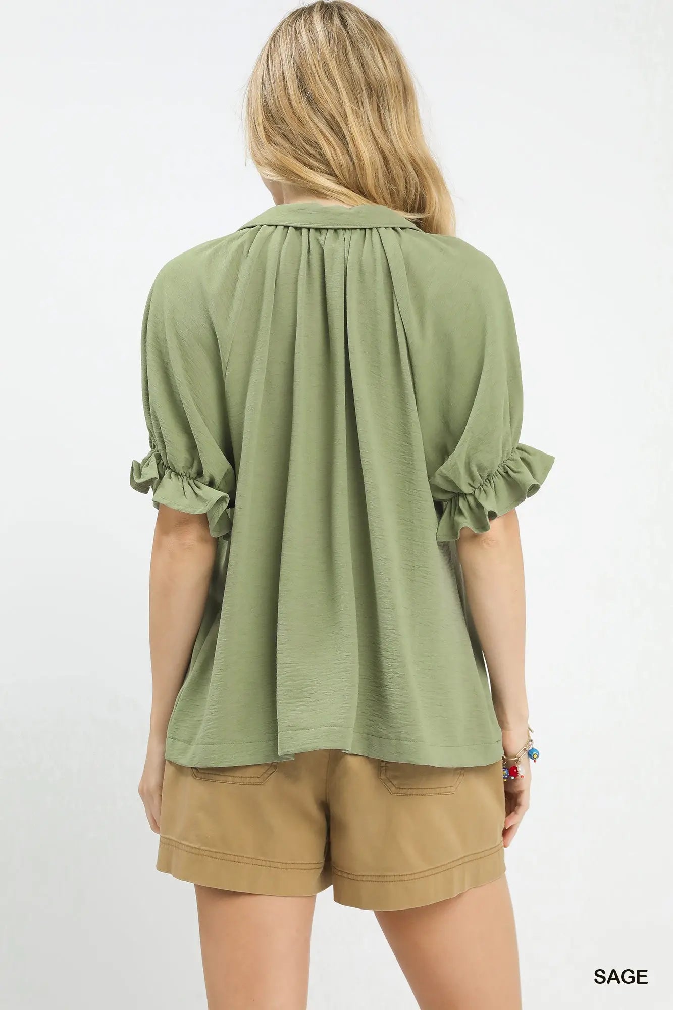 Woman wearing a green blouse with rolled-up sleeves and beige shorts on a white background