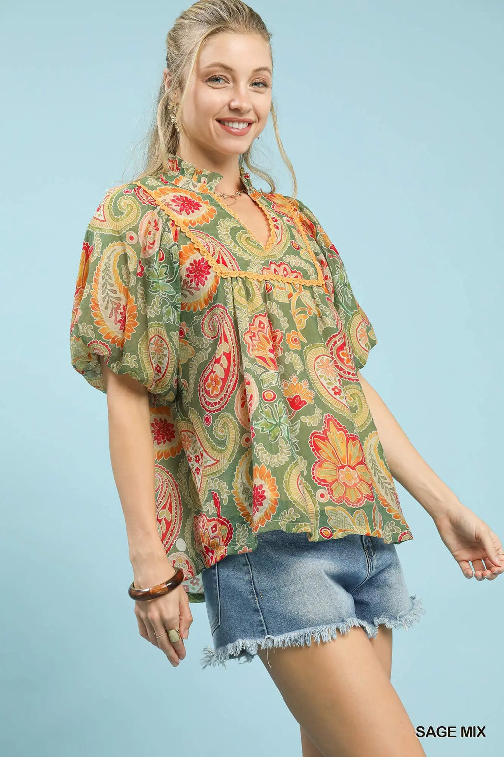 Woman wearing a colorful paisley blouse with denim shorts on a light blue background