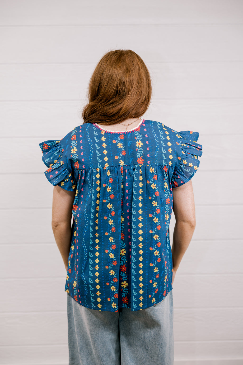 Person wearing a blue patterned blouse with ruffled sleeves against a white background