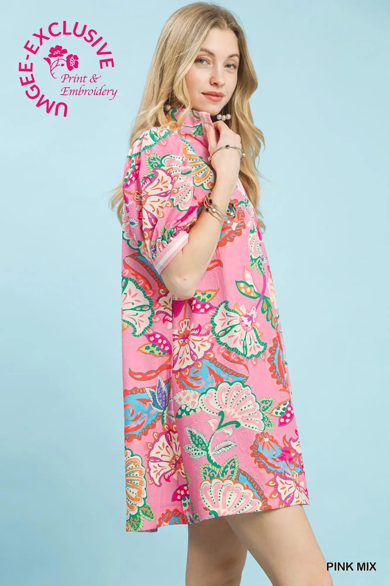 Woman wearing a colorful kimono-style dress with 'UMgee Exclusive' branding on a light blue background.