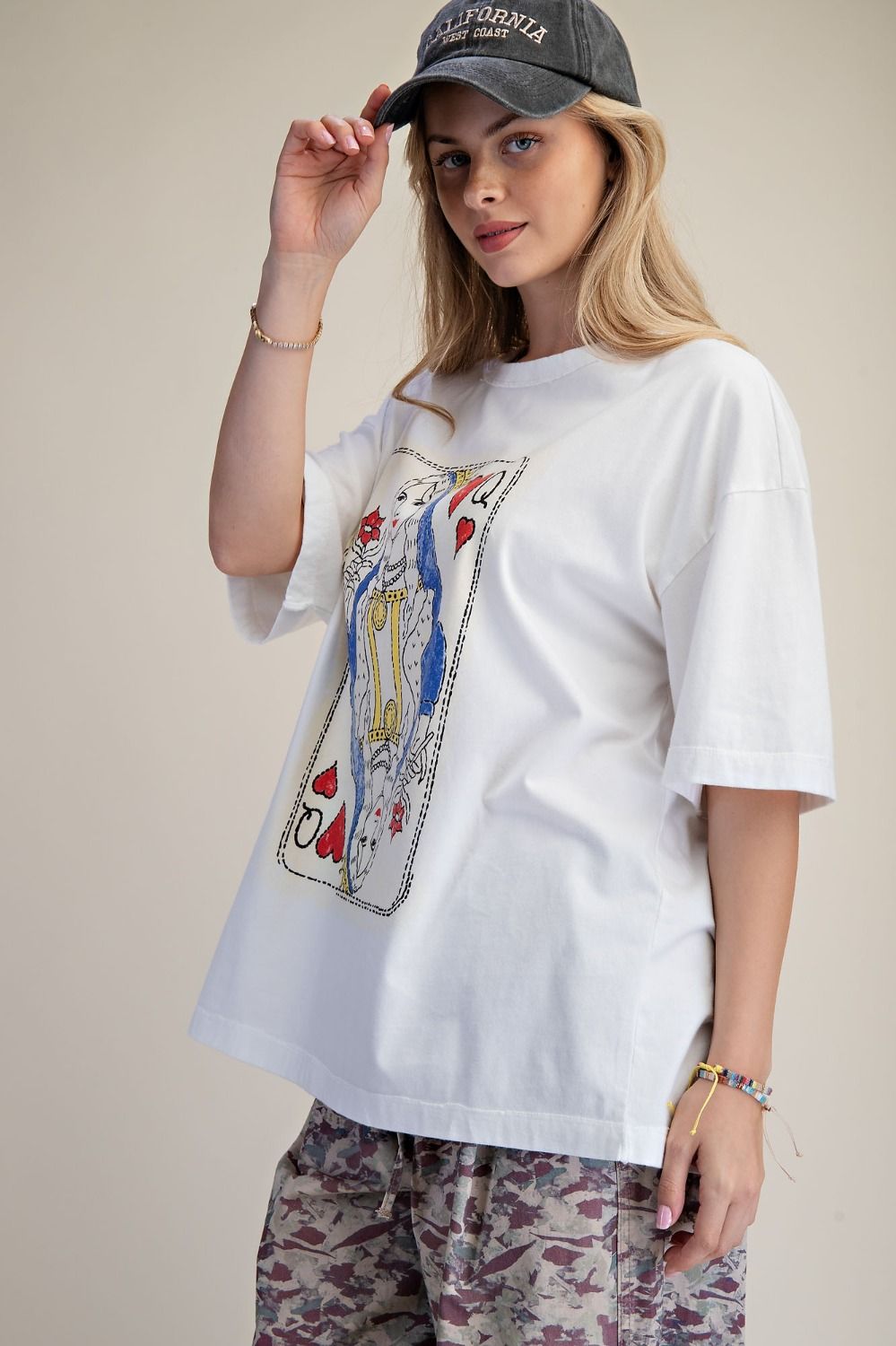 Person wearing a white t-shirt with a graphic design and a cap, standing against a plain background