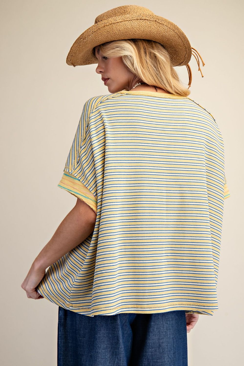 Person wearing a yellow and blue striped shirt with a cowboy hat on a beige background