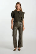 Woman wearing a dark green top with a bow detail and leather pants on a white background