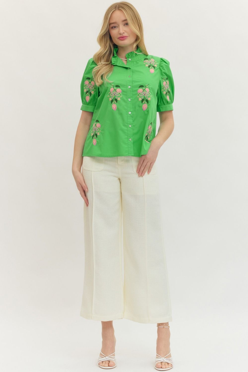 Woman wearing a green embroidered blouse and white pants on a white background