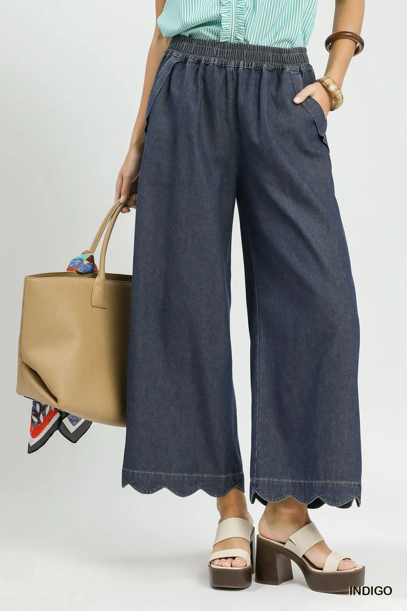 Person wearing blue wide-leg pants holding a beige handbag on a light gray background