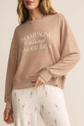 Person wearing a beige sweatshirt with text and light-colored pants with patterns.