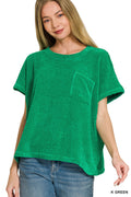 A woman wearing a bright green waffle-knit short-sleeve top with a chest pocket, paired with blue jeans, against a plain white background.